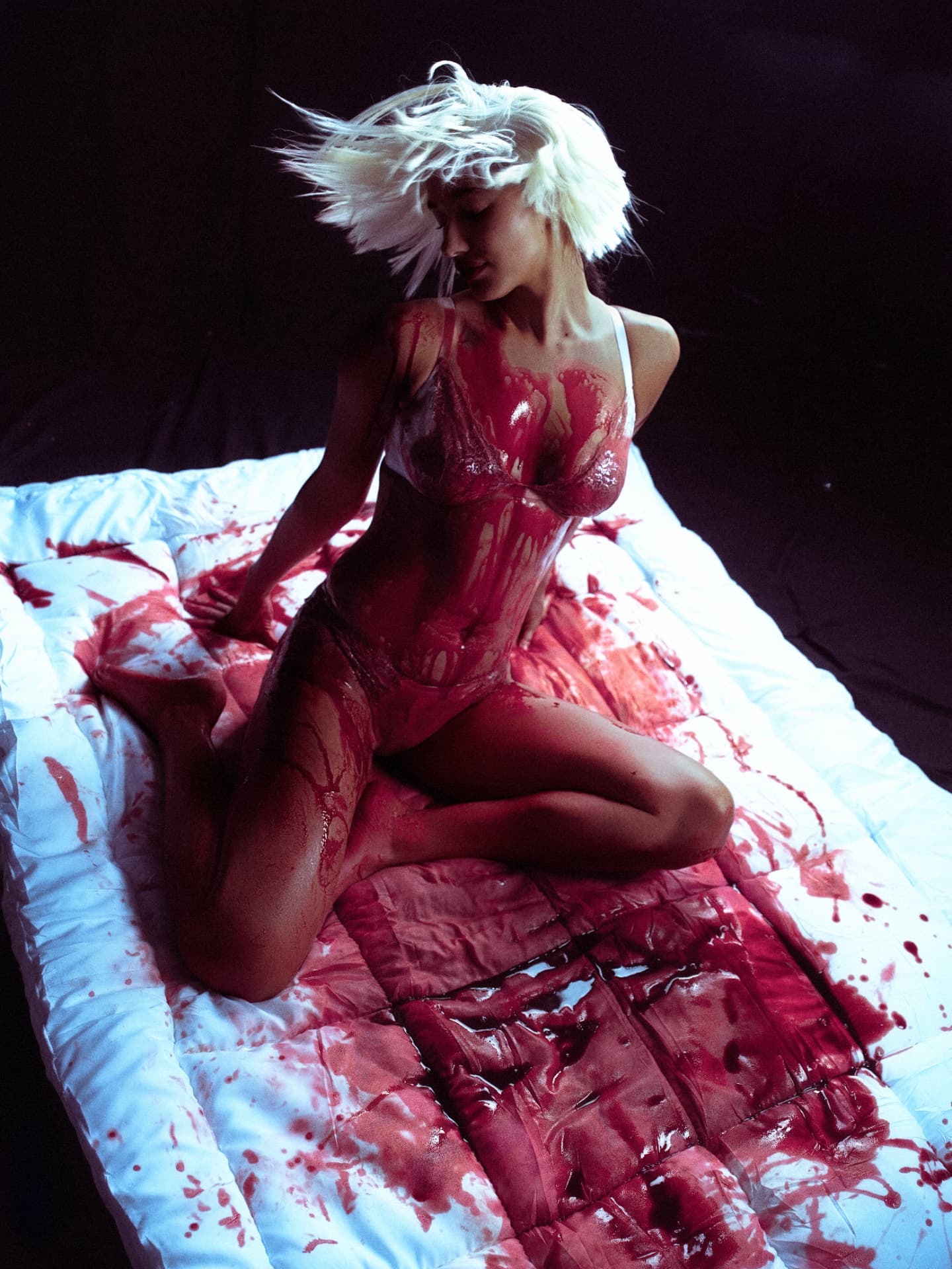 Delilah kneeling on a white quilt, crimson-soaked