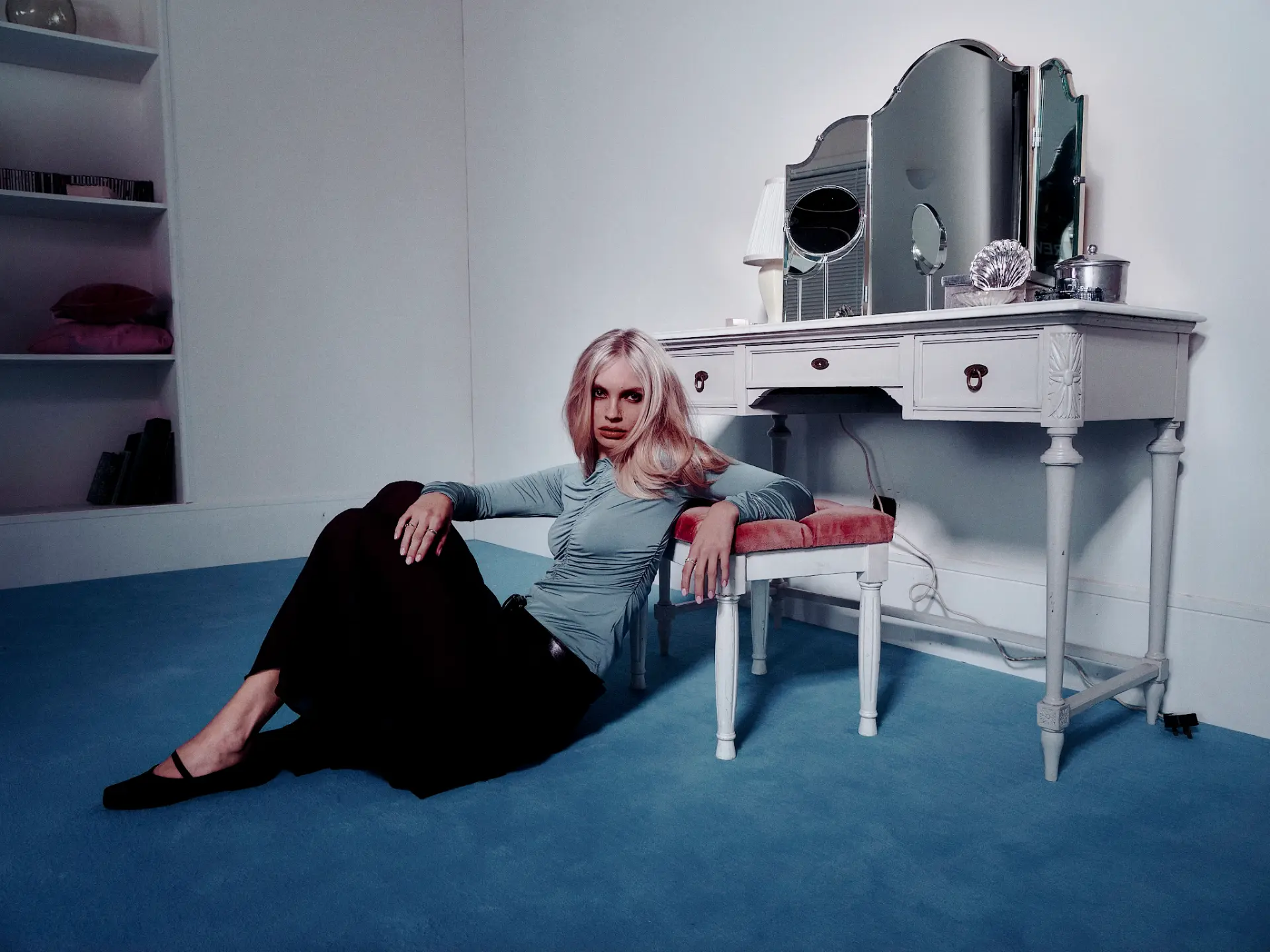 Model seated on the floor beside a white dressing table