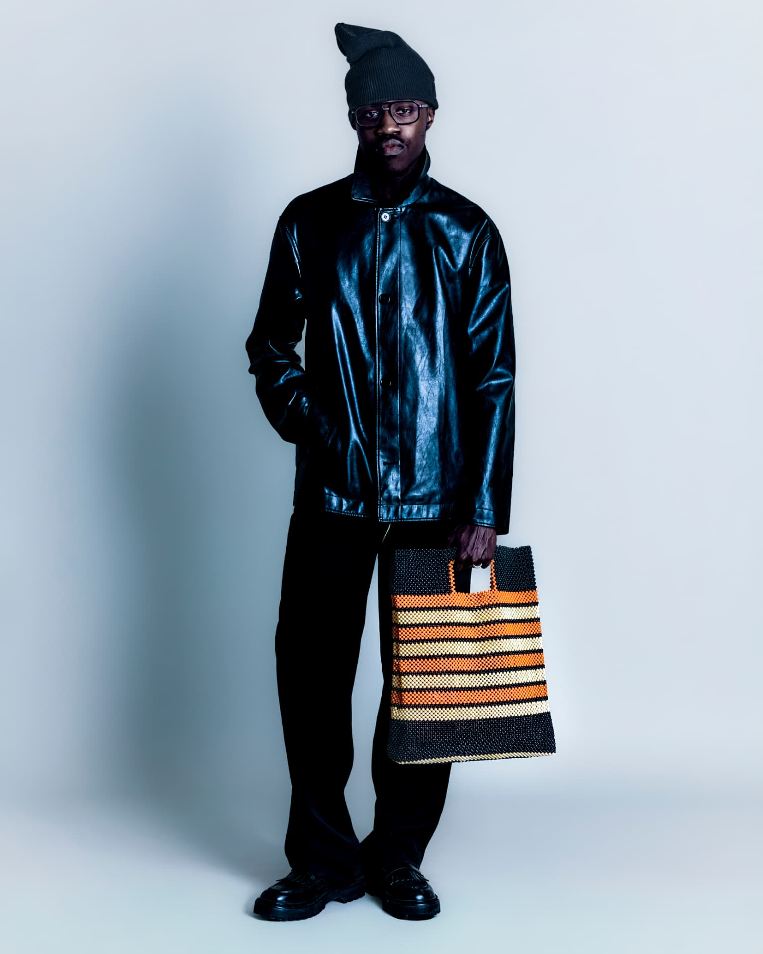 Model in black leather holding a striped beaded tote