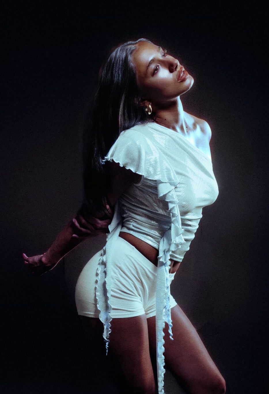 Delilah in pale ruffled knitwear under a hard studio light