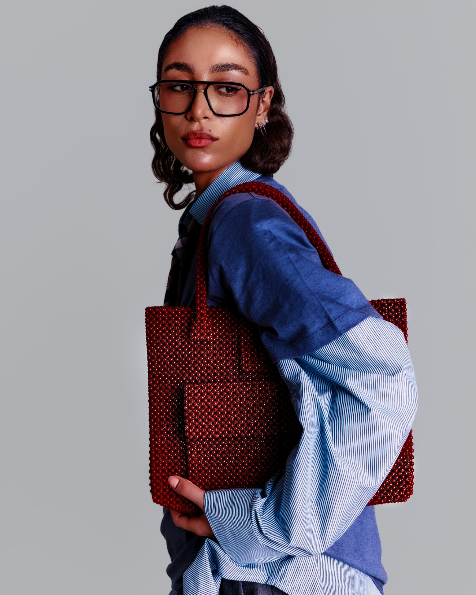 Red beaded tote carried over the shoulder in blue shirting